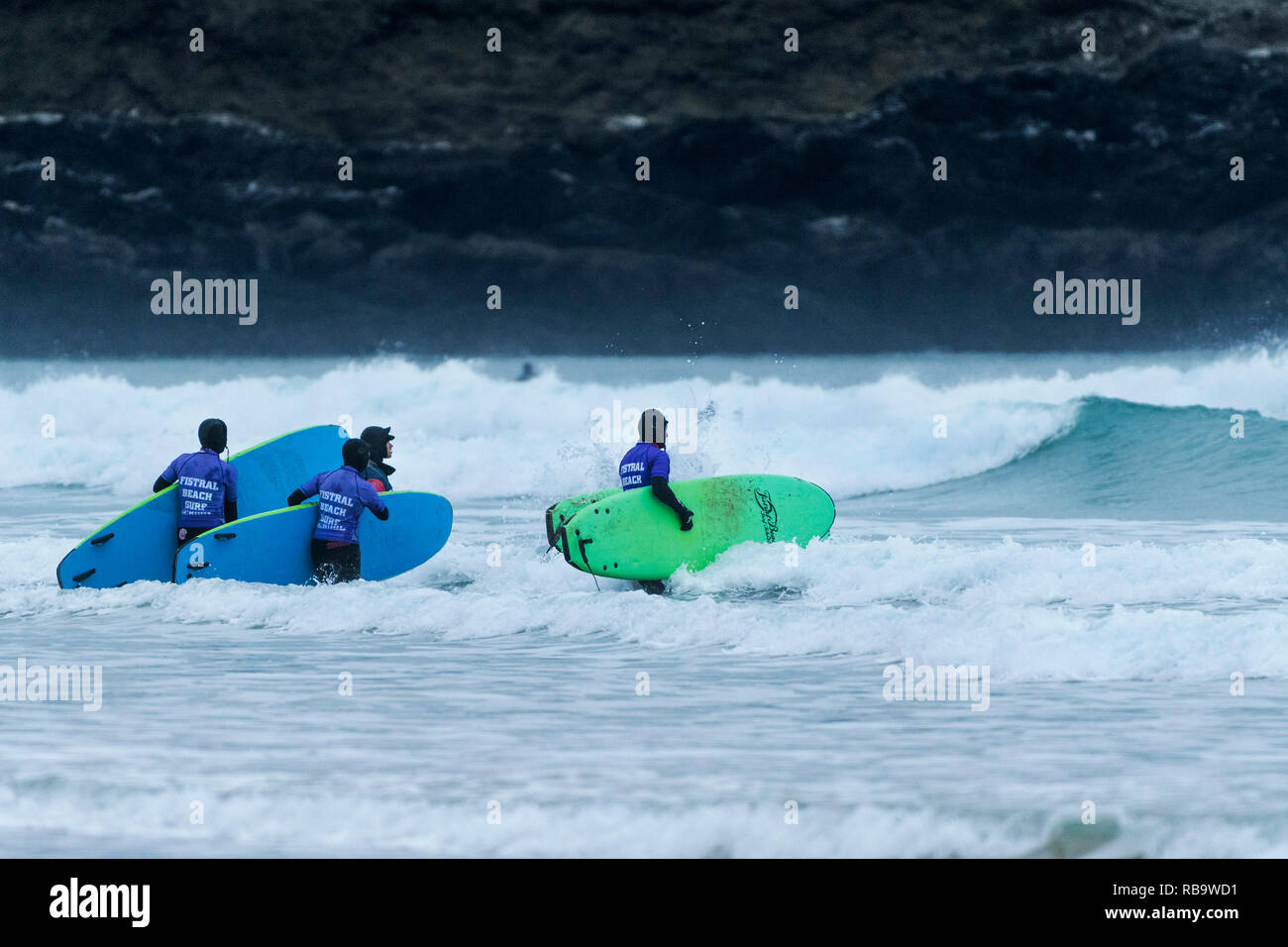 Les surfeurs débutants avec leurs planches de surf et de marcher dans la mer pour une leçon de surf à la plage de Fistral Newquay en Cornouailles. Banque D'Images
