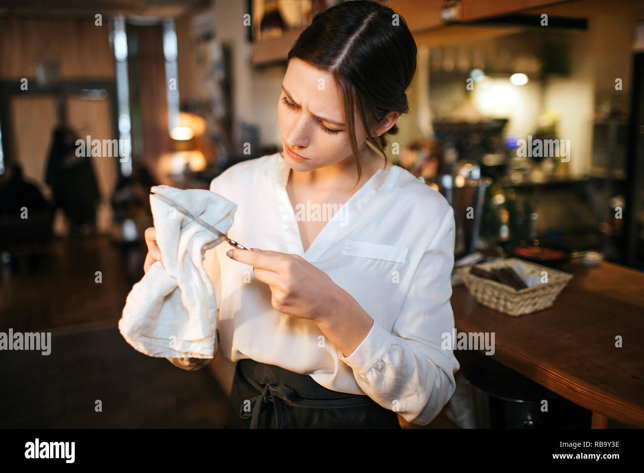 Jeune serveuse occupé stand au bar et essuyez le couteau. Elle l'examiner attentivement. Femme travail dans restaurant Yougn Banque D'Images