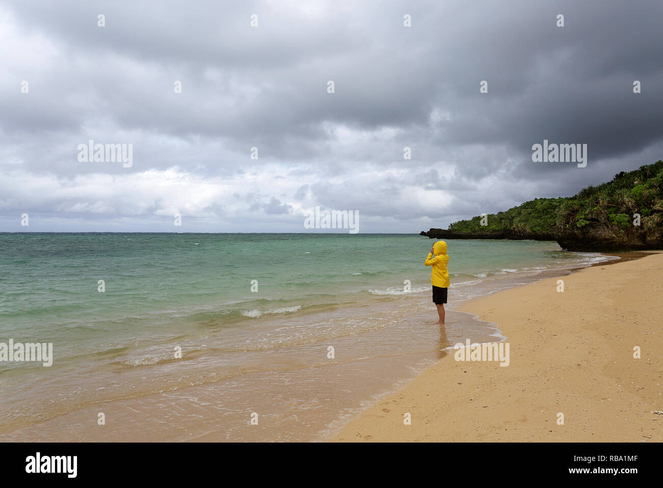 Jeune femme en veste jaune debout, marcher dans l'eau peu profonde sur une belle plage isolée, Ishigaki, Japon Banque D'Images