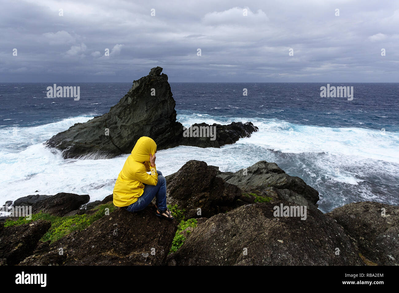 Woman in yellow jacket gel sur un rocher à la recherche à l'état de la mer sur la côte sauvage à Uganzaki dans le phare de l'Île Ishigaki, Japon Okinawa Banque D'Images
