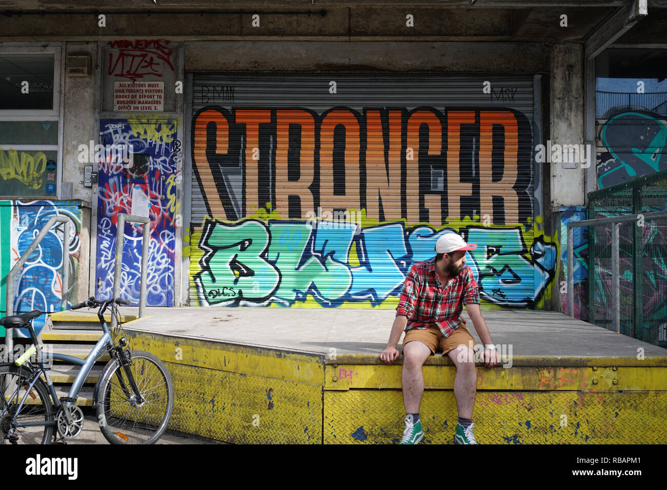 Un homme de 23 ans assis en face de graffitis. Banque D'Images