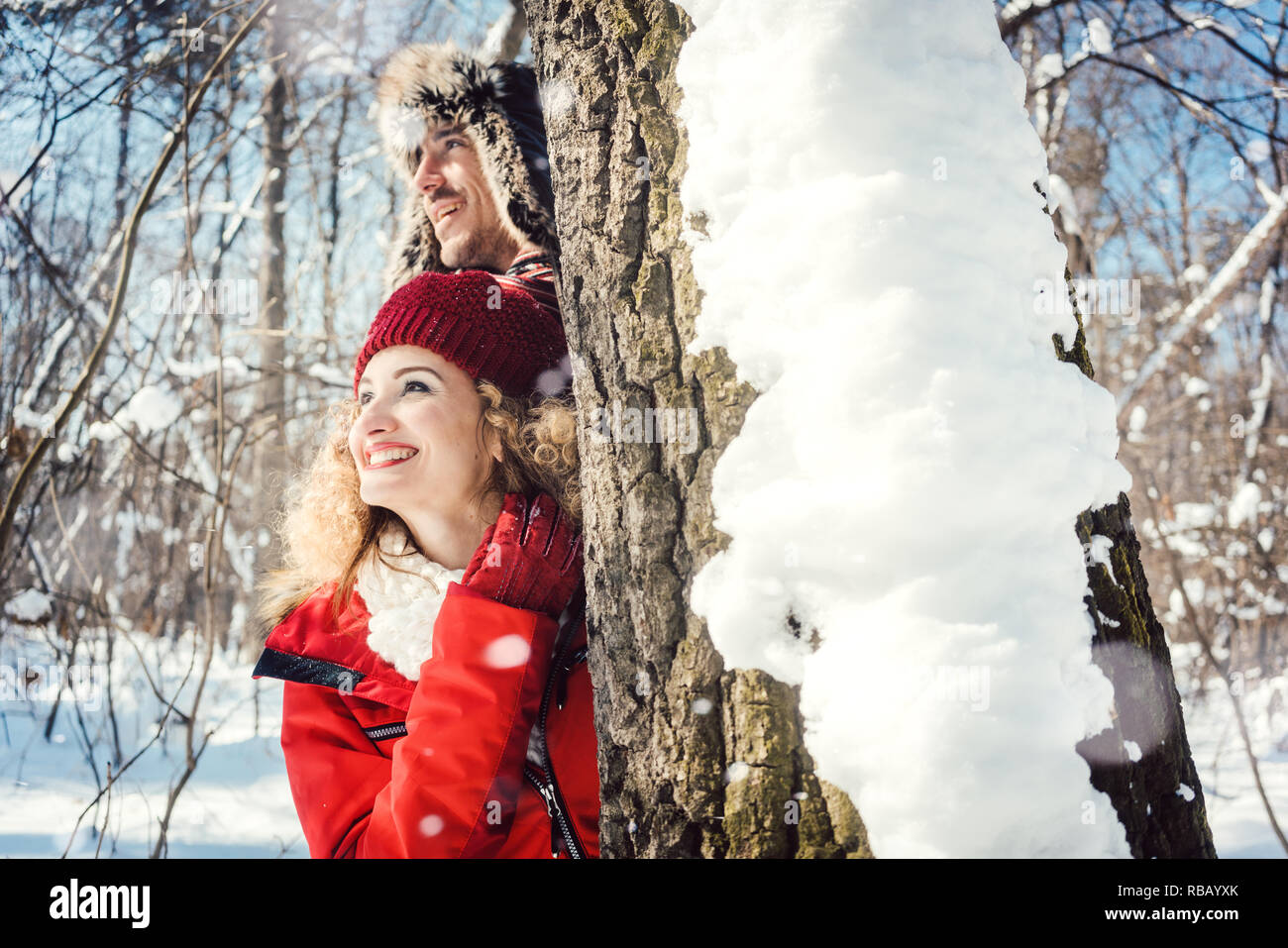 Playful couple se cacher derrière un tronc d'arbre dans la neige Banque D'Images