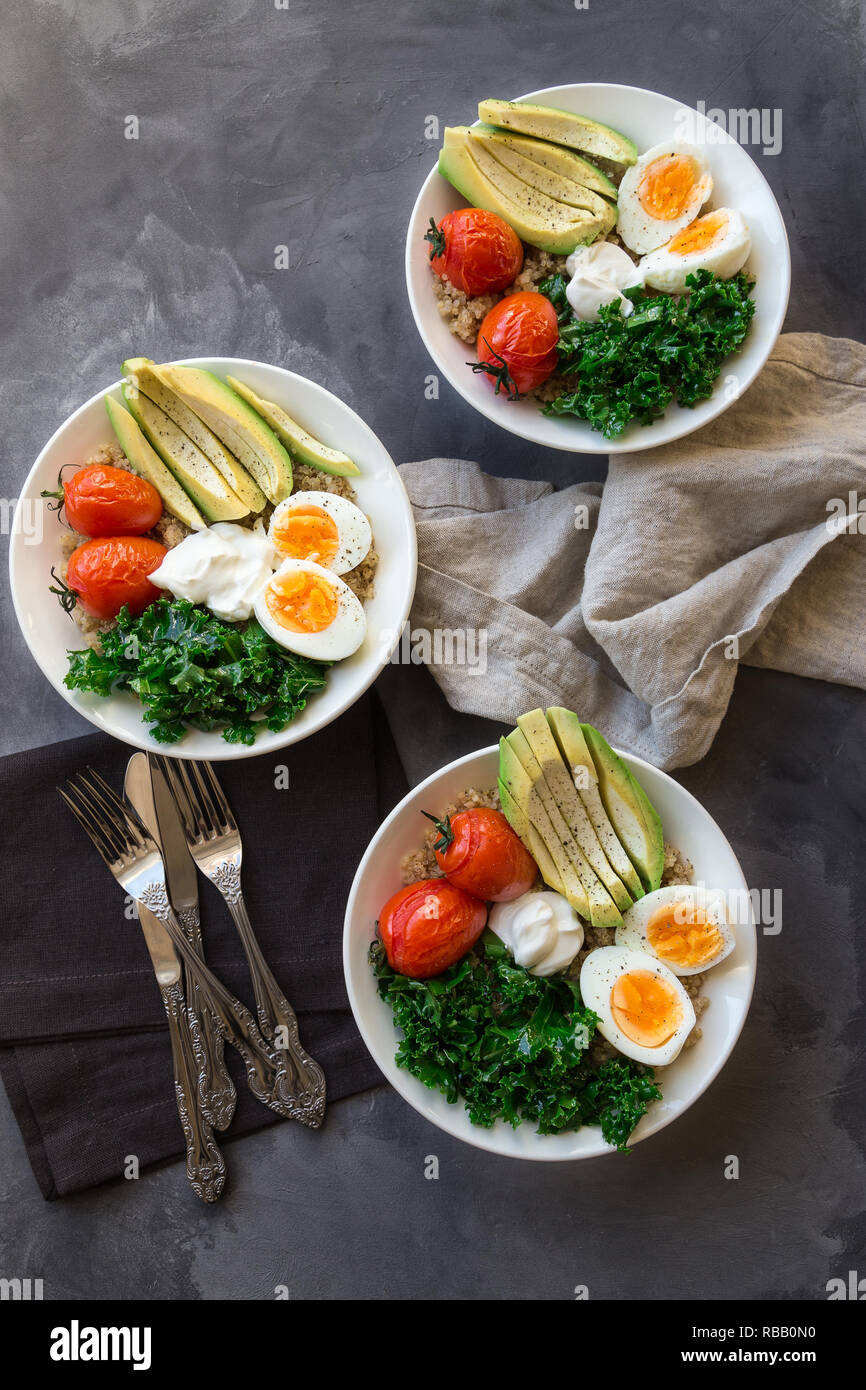 Le quinoa cuit avec des bols de bouddha les tomates, l'avocat, le chou vert, œufs durs et du yaourt grec sur fond de béton gris. Petit déjeuner sain. Vue d'en haut. Banque D'Images