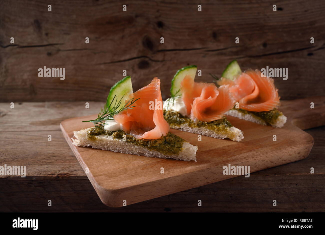 Dans une ligne de canapés de saumon fumé, concombre, pesto, crème et garnir d'aneth sur une planche de bois rustique, copy space, Close up, de mise au point sélectionnée et étroit Banque D'Images