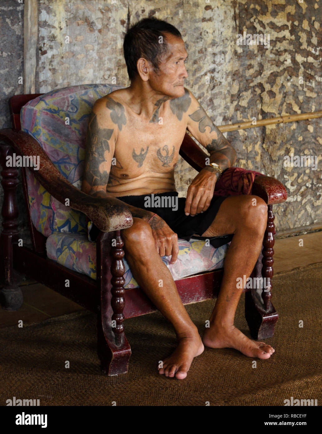 Personnes âgées Iban homme avec des tatouages tribaux sitting in chair en zone commune de Mengkak, Batang Ai Longhouse, Sarawak (Bornéo), Malaisie Banque D'Images