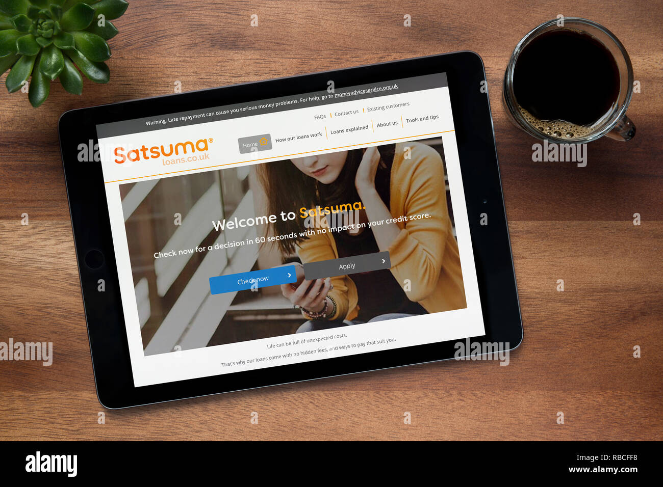 Le site web de Satsuma prêts est vu sur une tablette iPad, sur une table en bois avec une machine à expresso et d'une plante (usage éditorial uniquement). Banque D'Images