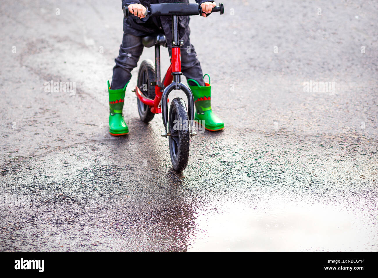 Suspendre le vélo vert et des bottes de caoutchouc et une flaque d'eau. L'enfance Banque D'Images