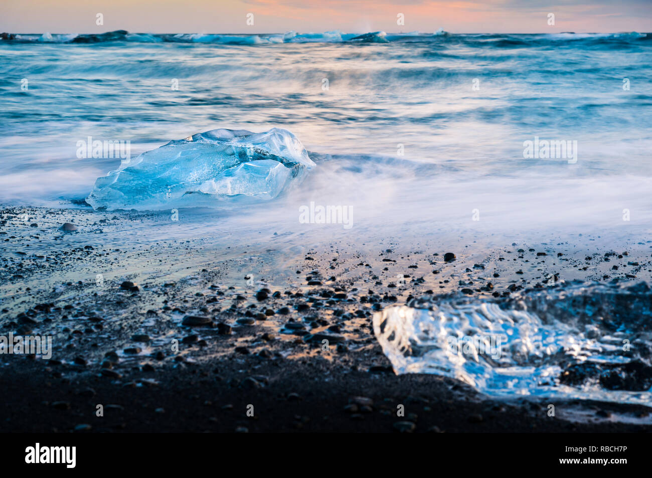 Éclaboussures des vagues de glace sur la plage du Diamant en Islande pendant le coucher du soleil Banque D'Images