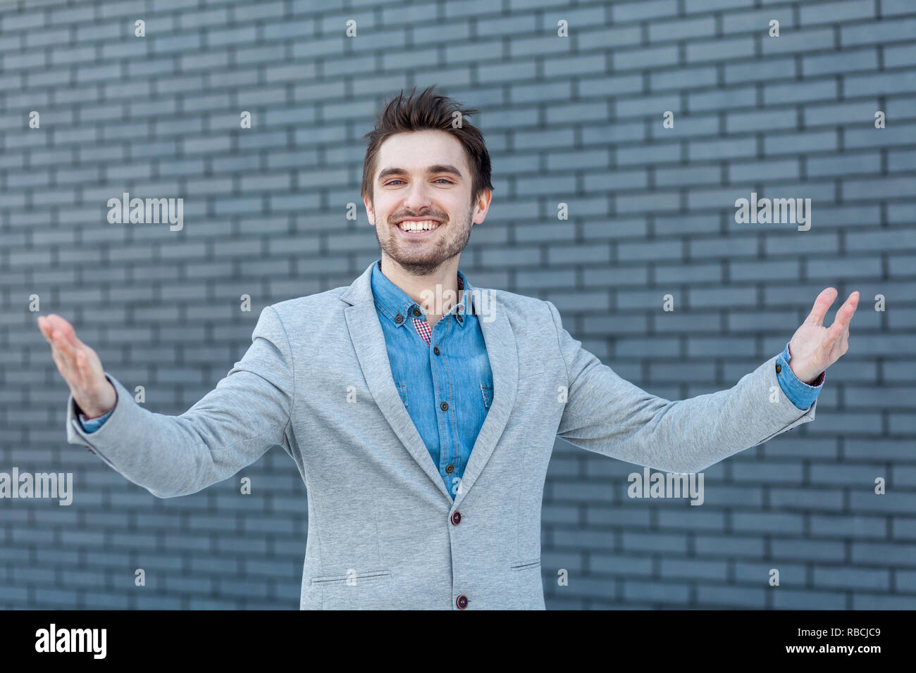 Portrait of happy beau barbu dans un style décontracté avec dents sourire permanent et les bras levés, looking at camera. Piscine studio shot sur mur de brique Banque D'Images