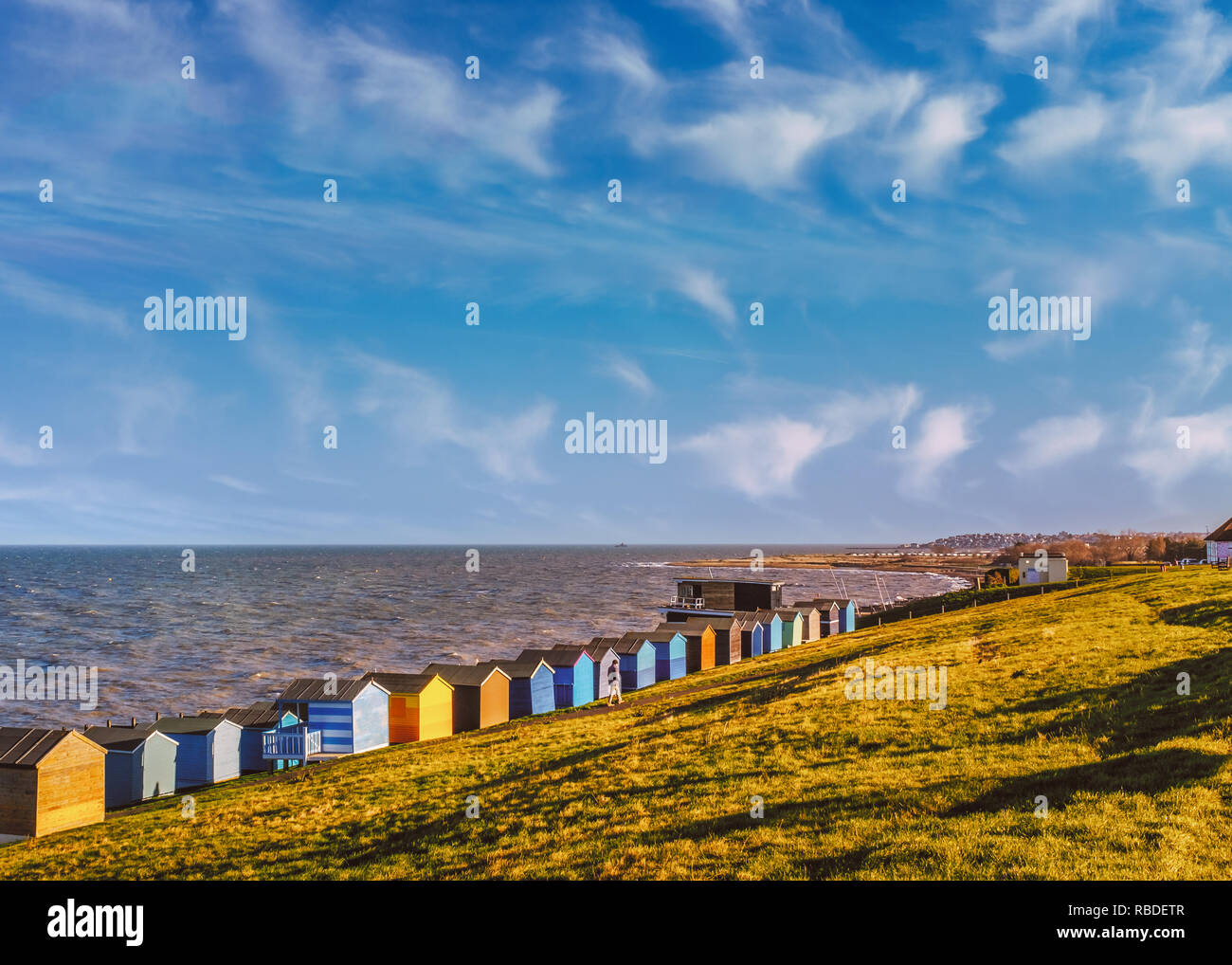 Rangée de cabines de plage le long de la côte à Whitstable, Tankerton, Kent. L'herbe verte pentes sont derrière les baraques et un homme se promener le long de l'herbe. L Banque D'Images