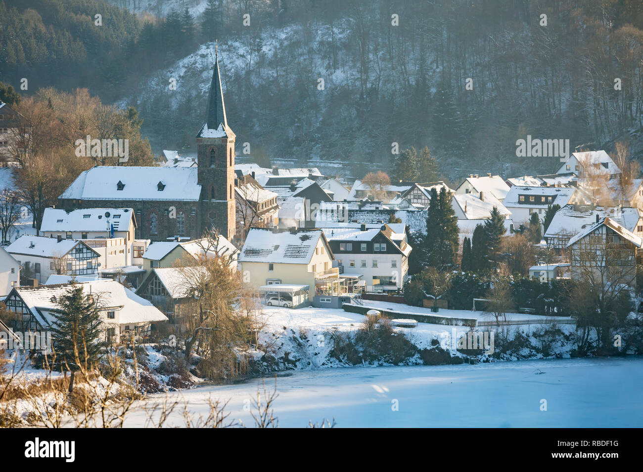 Vue sur le lac gelé de Rursee l'église et village de Einruhr avec de la neige en hiver, dans l'Eifel, en Allemagne. Banque D'Images