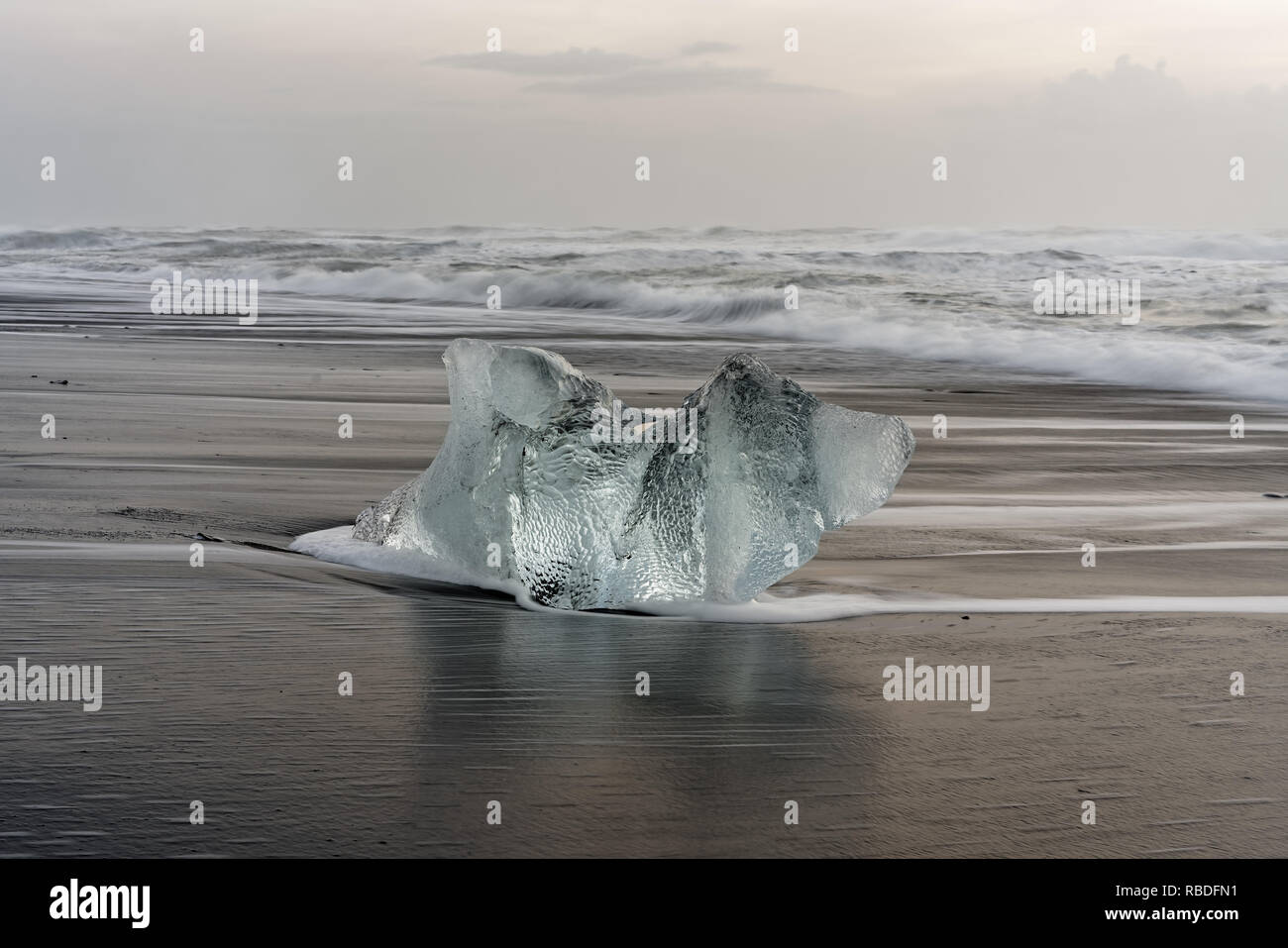 Substitution, bloc de glace sur une plage noire avec surf, avec l'eau de retour la réflexion sur le sable humide, les vagues roulant dans l'arrière-plan - Localisation : Islande Banque D'Images