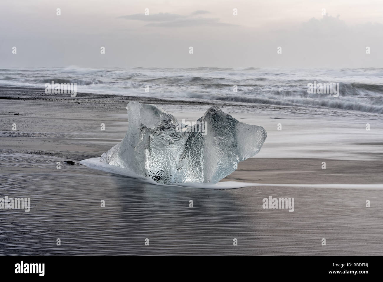 Substitution, bloc de glace sur une plage noire avec surf, avec l'eau de retour la réflexion sur le sable humide, les vagues roulant dans l'arrière-plan - Localisation : Islande Banque D'Images