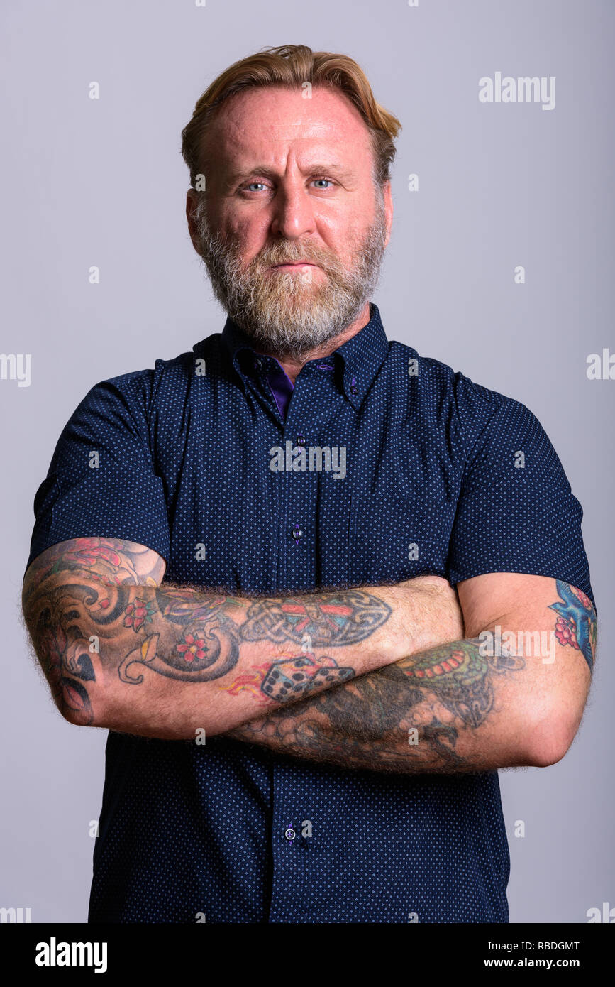 Homme barbu d'âge mûr avec des tatouages à la main avec les bras croisés en gris b Banque D'Images