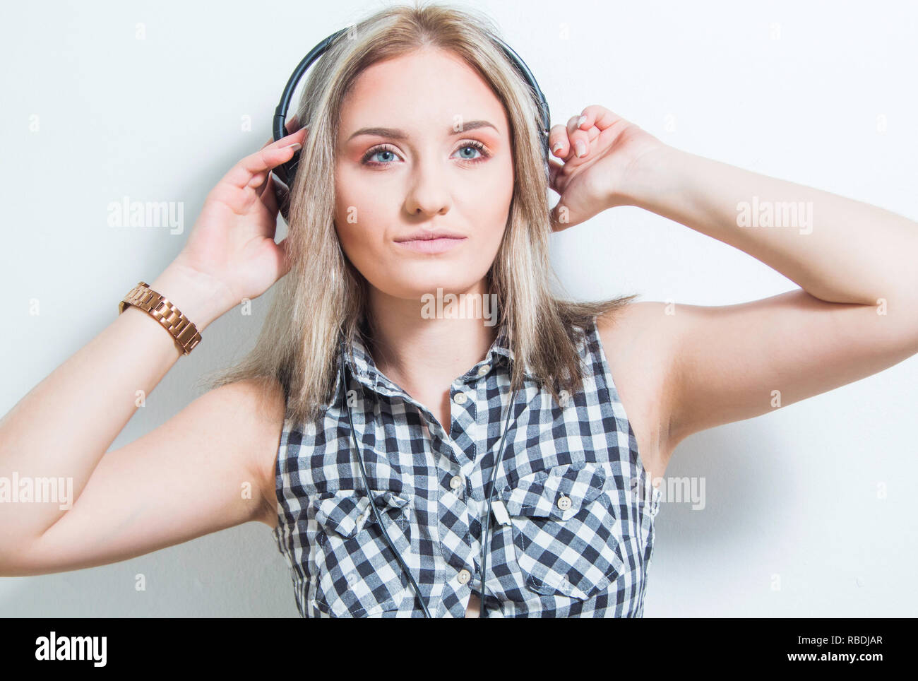 Belle jeune fille en chemise à carreaux avec des écouteurs et smart phone profiter de la musique à la maison, la tête et épaules corps portrait. Mur Blanc, les jeunes mu Banque D'Images