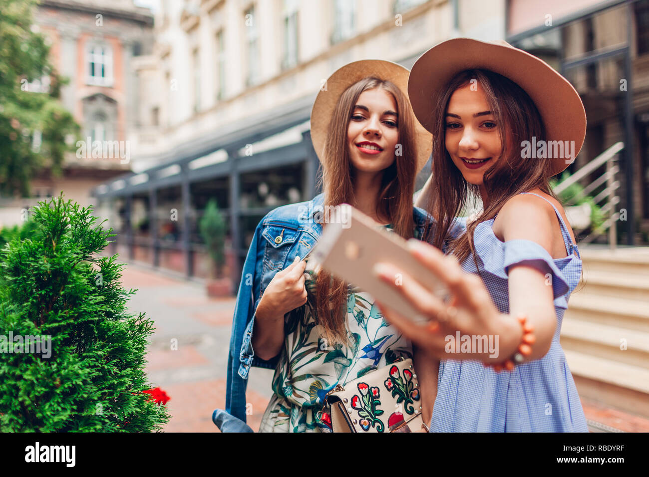 Outdoor portrait de deux jeunes femmes à la mode belle en tenant à l'aide de selfies téléphone. Happy girls having fun in ville. Meilleurs amis porter un chapeau Banque D'Images