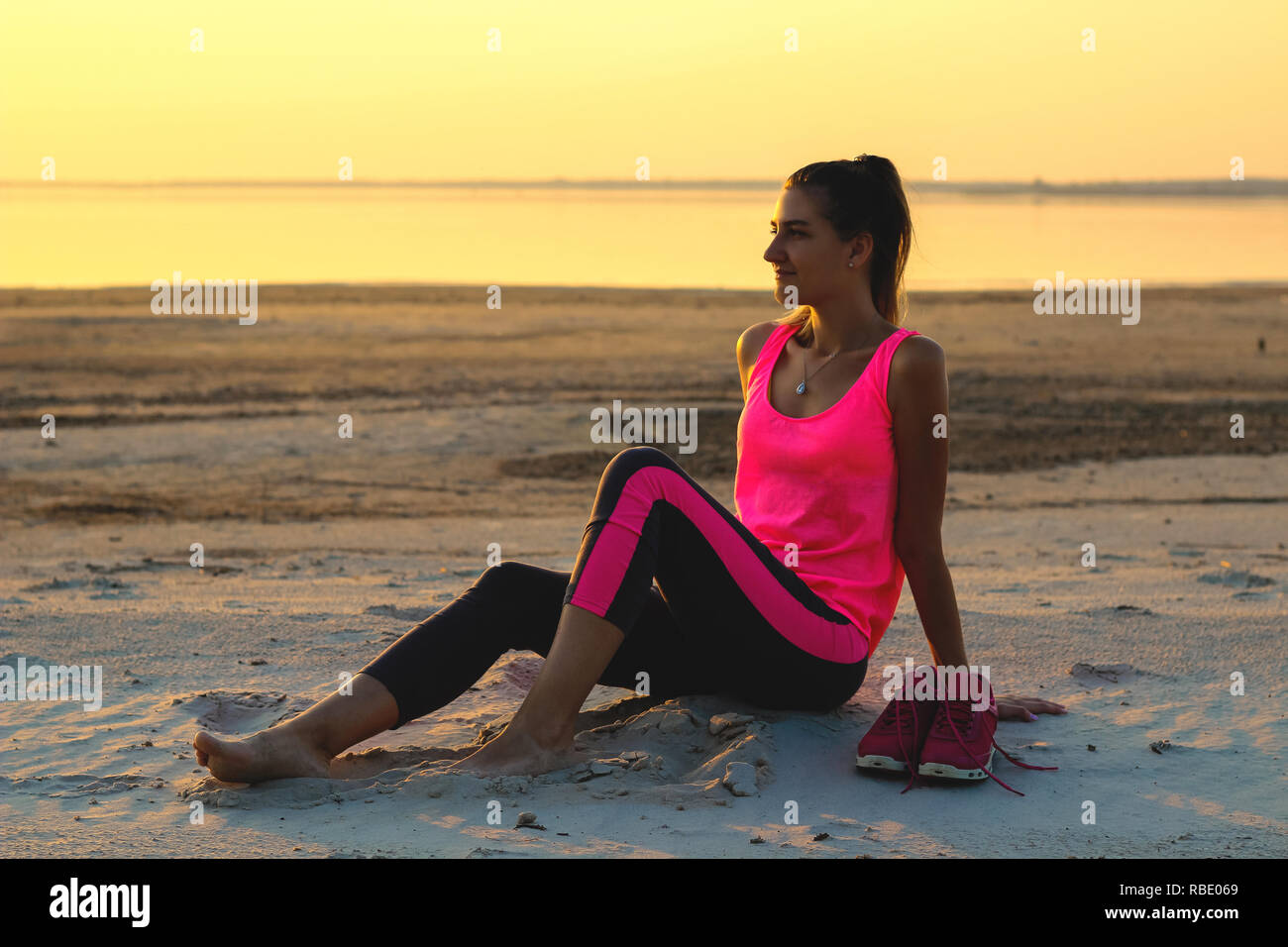 Jeune fille belle dans les vêtements de sport est situé sur une plage de  sable et bénéficie d'un coucher du soleil orange par la mer Photo Stock -  Alamy