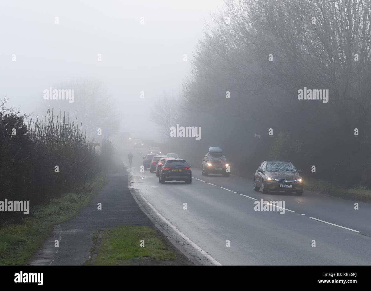 Un cycliste sans lumières presque disparaître dans le brouillard sur une route très fréquentée près de Glasgow en Ecosse, Royaume-Uni, l'Europe. Banque D'Images