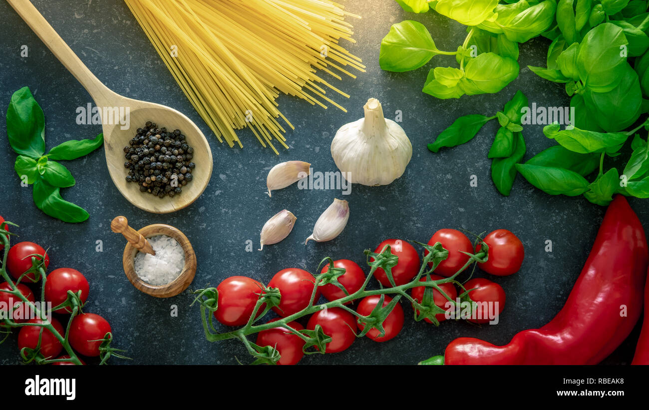 Ingrédients de cuisine italienne. Les pâtes spaghetti, tomates, basilic, l'ail et l'assaisonnement épices sur pierre sombre arrière-plan. Banque D'Images