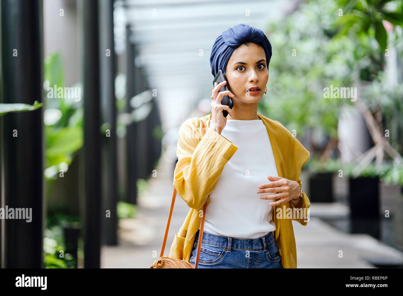 Une jeune et belle femme du Moyen-Orient dans un turban hijab fronce comme elle parle sur son smartphone dans la rue pendant la journée. Elle a l'air inquiet. Banque D'Images