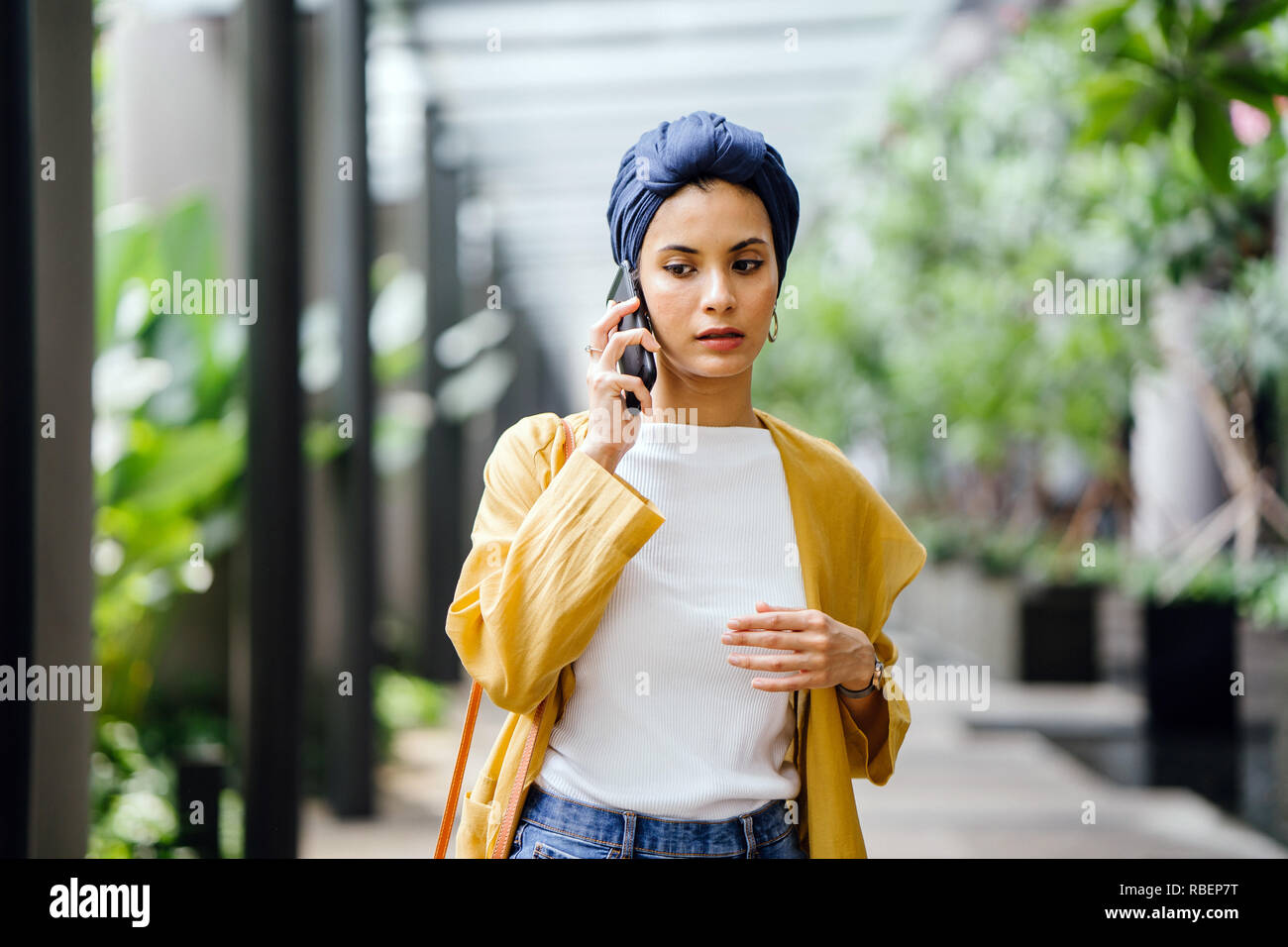 Une jeune et belle femme du Moyen-Orient dans un turban hijab fronce comme elle parle sur son smartphone dans la rue pendant la journée. Elle a l'air inquiet. Banque D'Images
