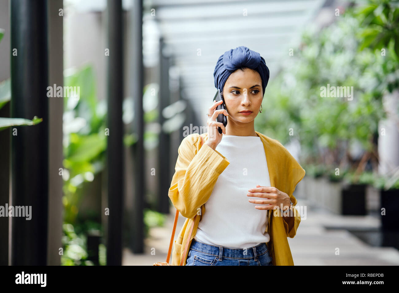 Une jeune et belle femme du Moyen-Orient dans un turban hijab fronce comme elle parle sur son smartphone dans la rue pendant la journée. Elle a l'air inquiet. Banque D'Images