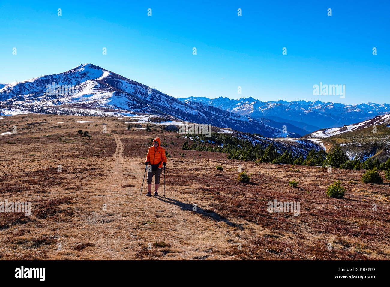 Walker femelle en orange Down jacket avec montagnes enneigées, Col de Pahlieres, Ax les Thermes, Ariège, Pyrénées, France Banque D'Images