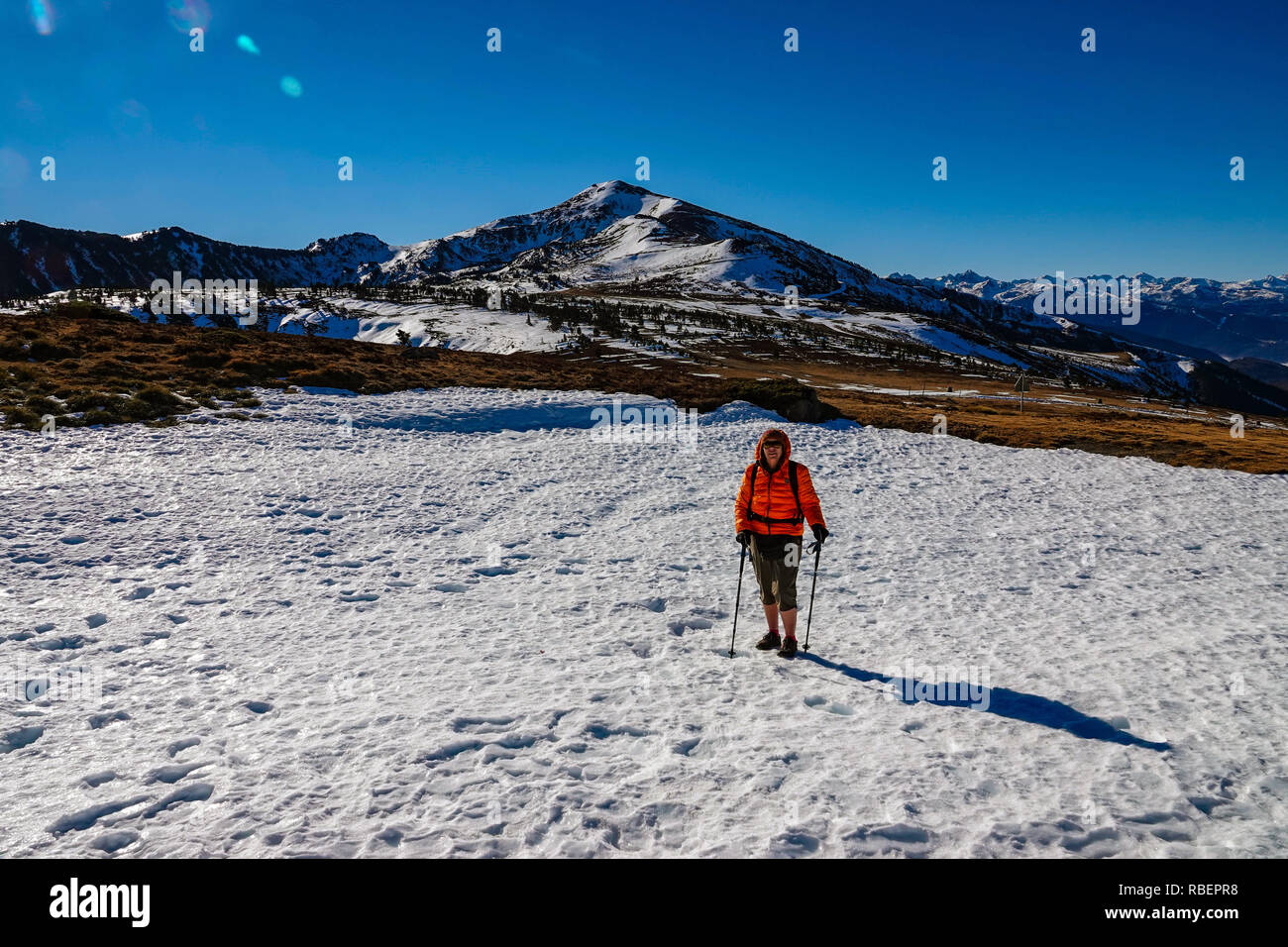 Walker femelle en orange Down jacket avec montagnes enneigées, Col de Pahlieres, Ax les Thermes, Ariège, Pyrénées, France Banque D'Images