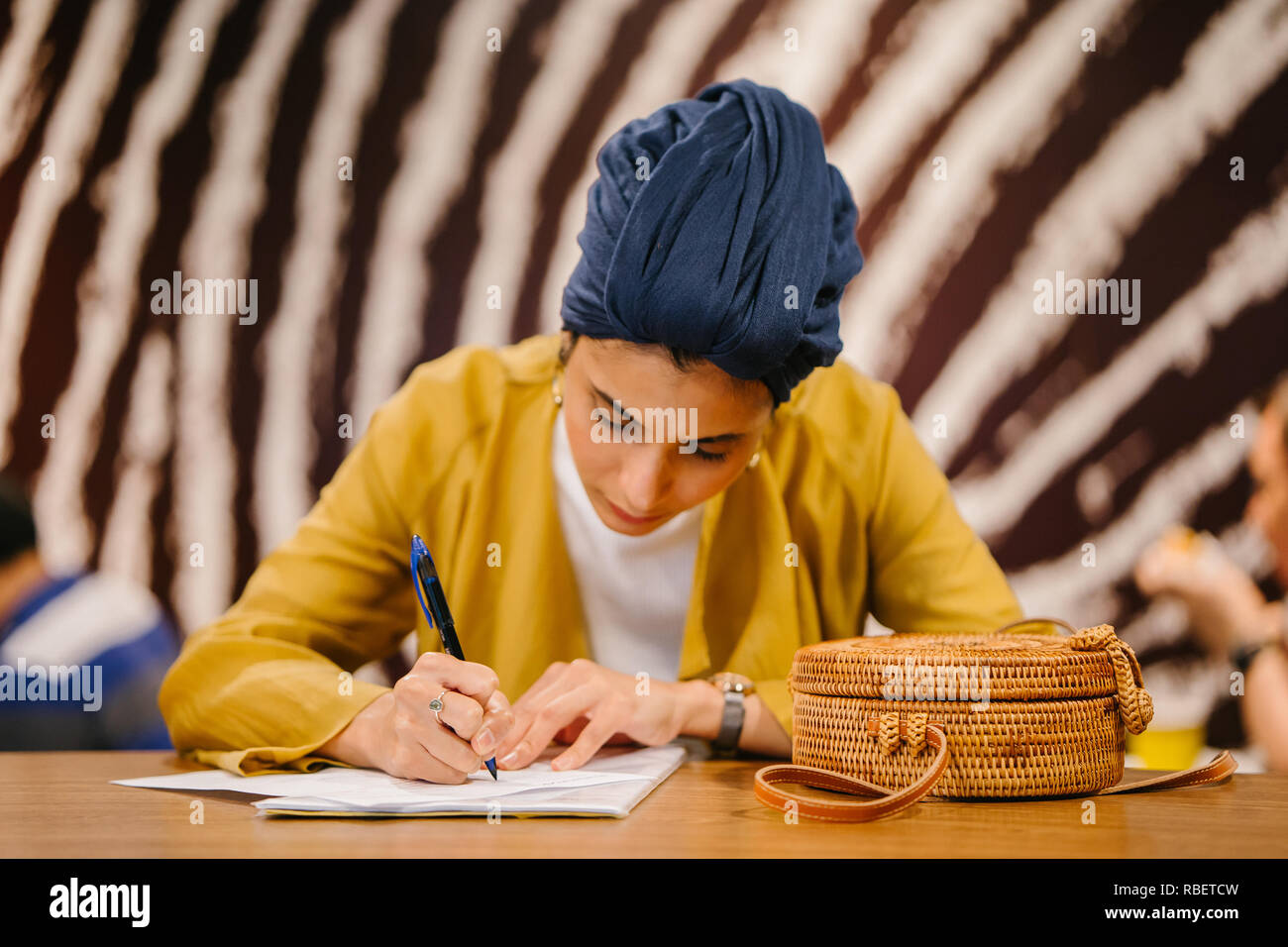 Portrait d'une charmante et élégante Middle Eastern woman écrit dans son journal, ordinateur portable. Elle porte un foulard hijab turban bleu. Banque D'Images