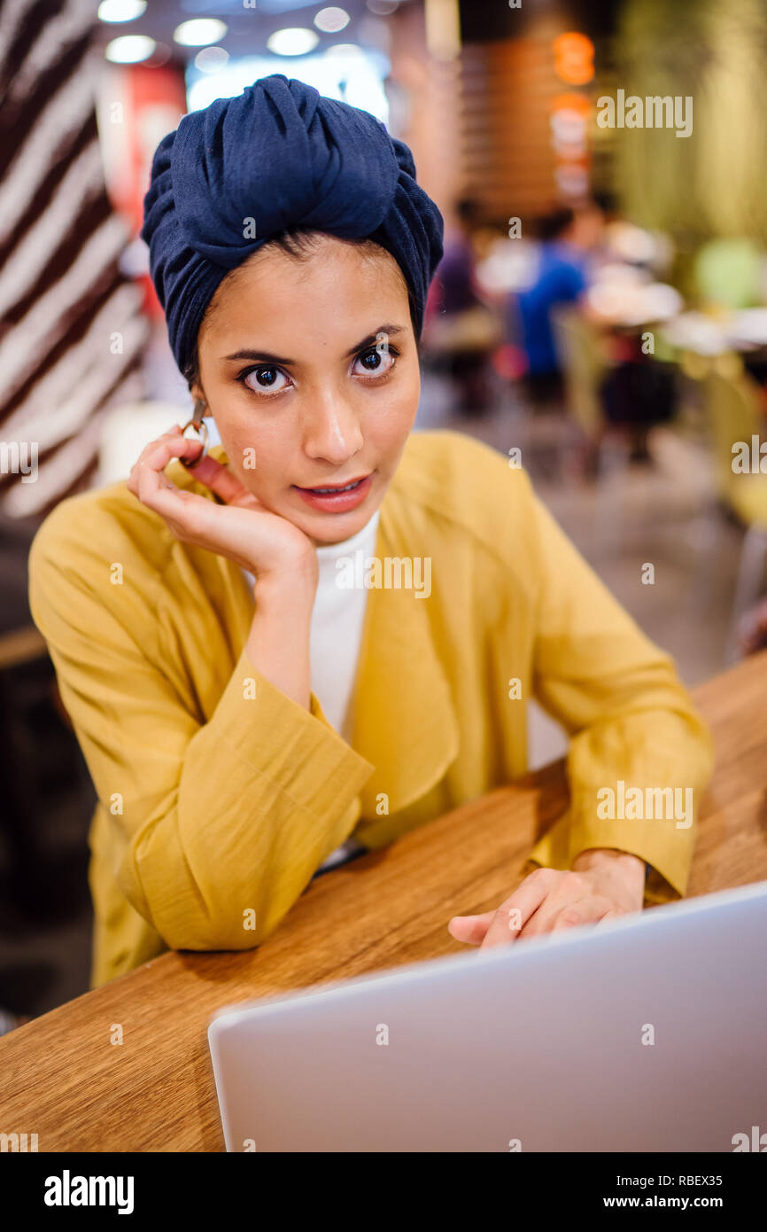 Une jeune femme asiatique malais est saisissant et travailler ou étudier sur son ordinateur portable dans un café pendant la journée. Elle porte un turban hijab. Banque D'Images