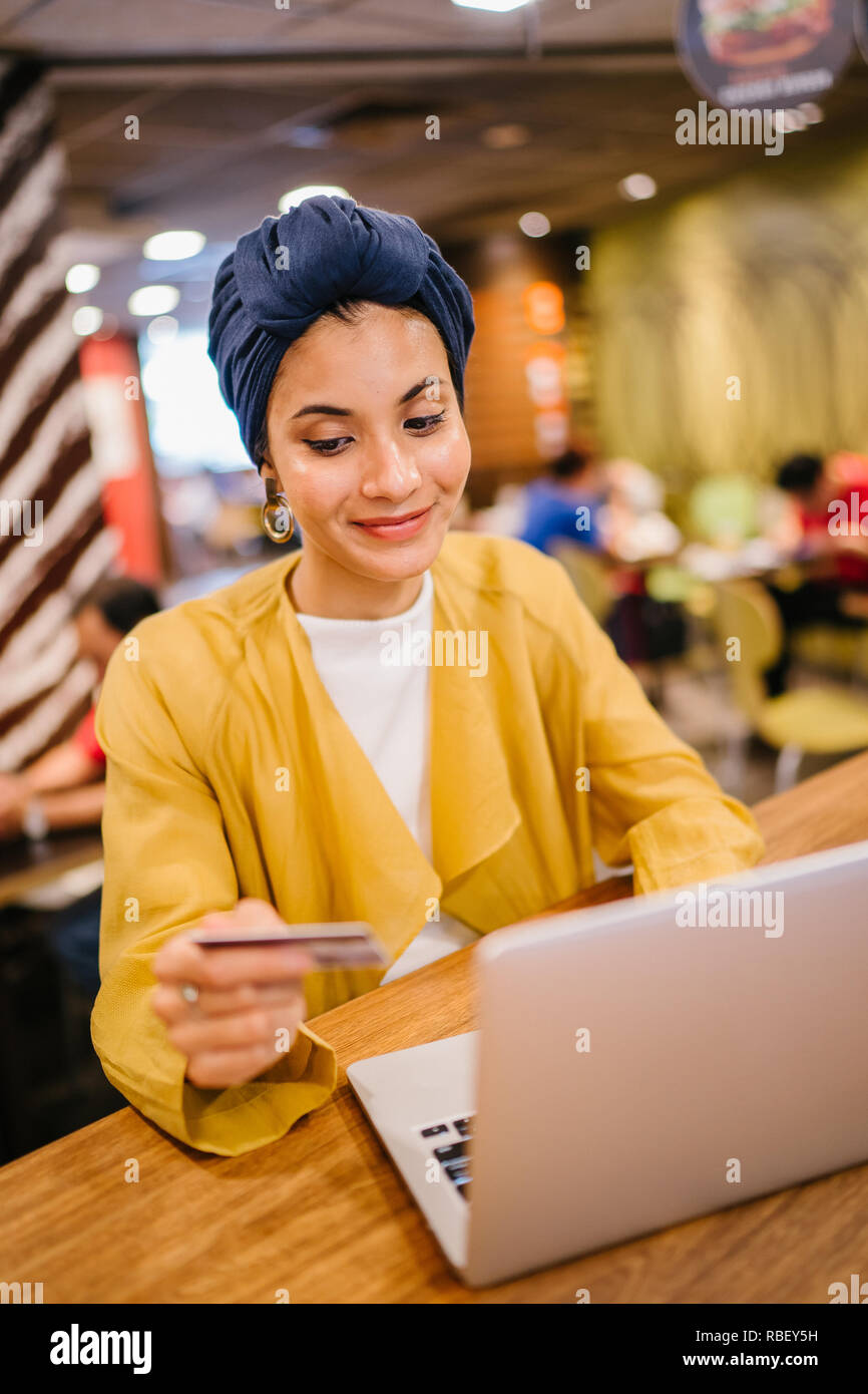 Portrait d'une jeune et belle femme musulmane malaise portant un turban de payer pour ses achats en ligne en ligne avec une carte de crédit sur son portable. Banque D'Images