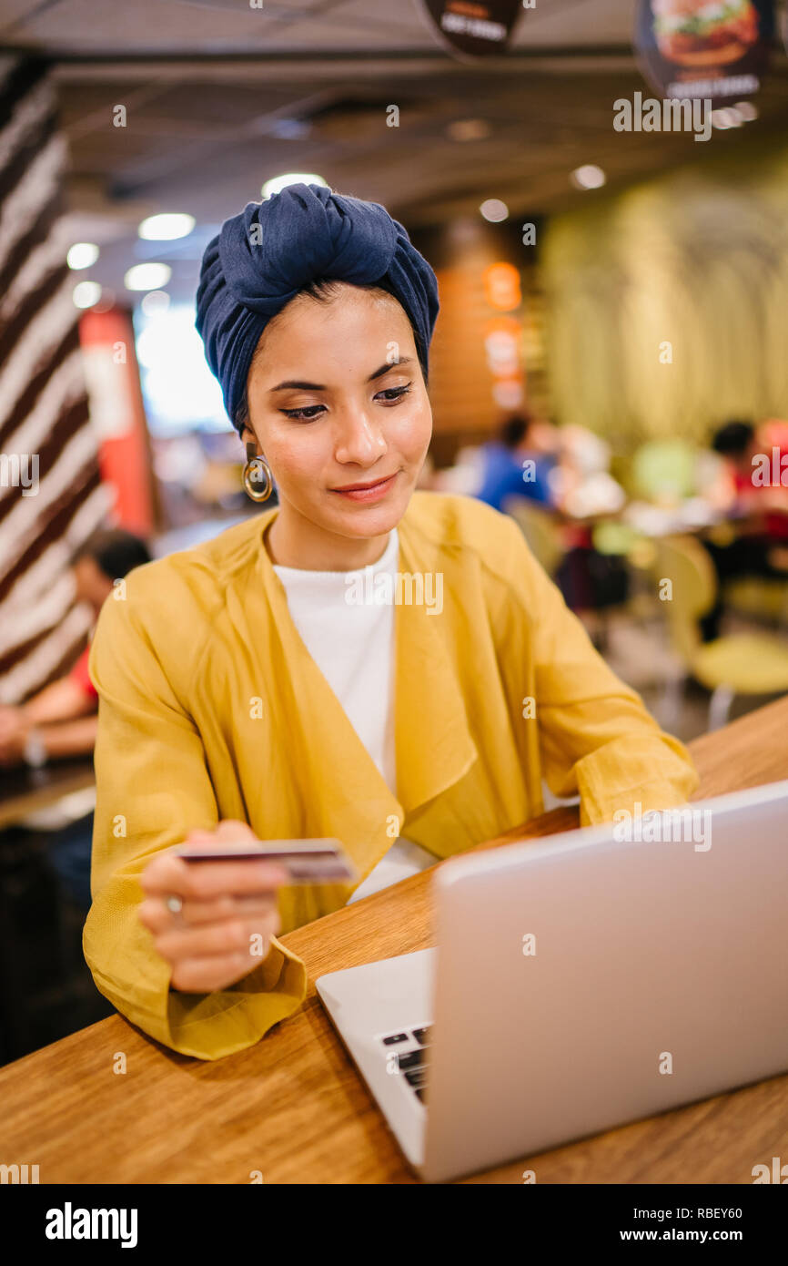 Portrait d'une jeune et belle femme musulmane malaise portant un turban de payer pour ses achats en ligne en ligne avec une carte de crédit sur son portable. Banque D'Images