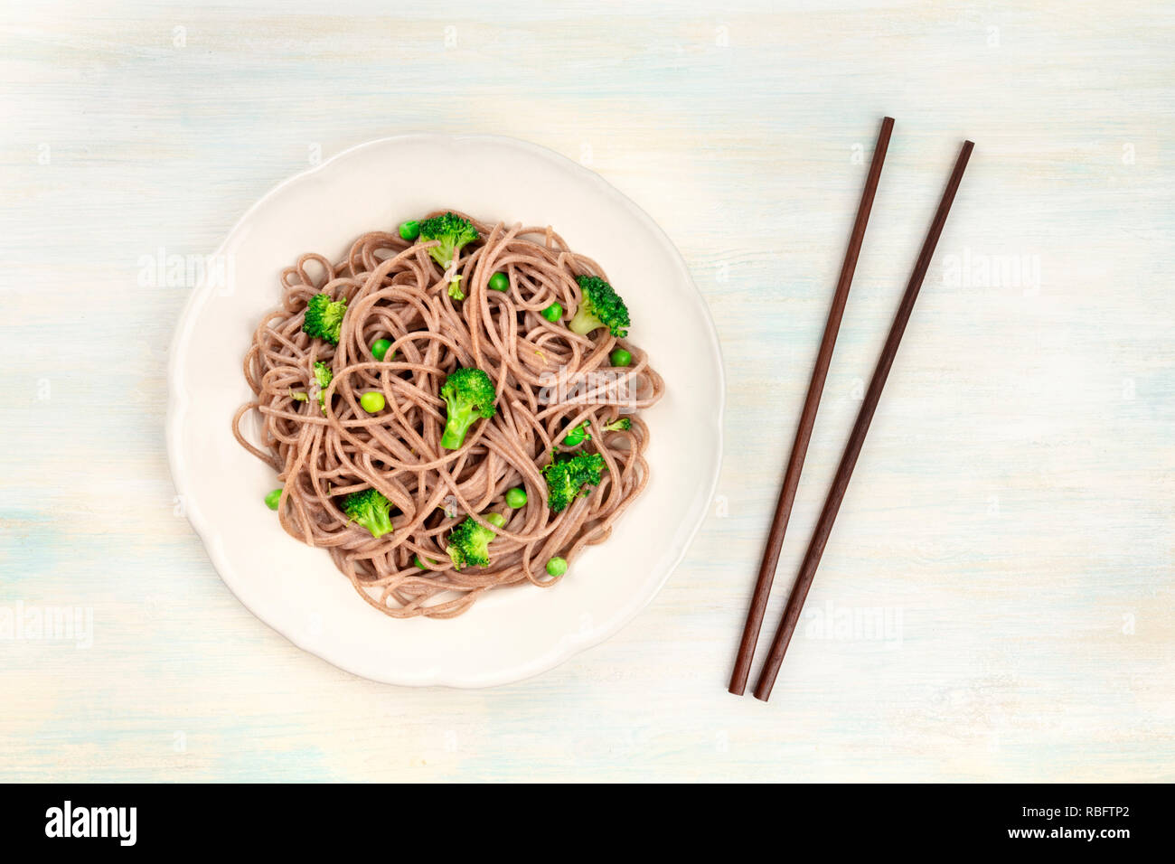 Un plat de Soba, nouilles de sarrasin avec des légumes verts, tourné par le haut sur un fond en bois clair avec des baguettes et copy space Banque D'Images