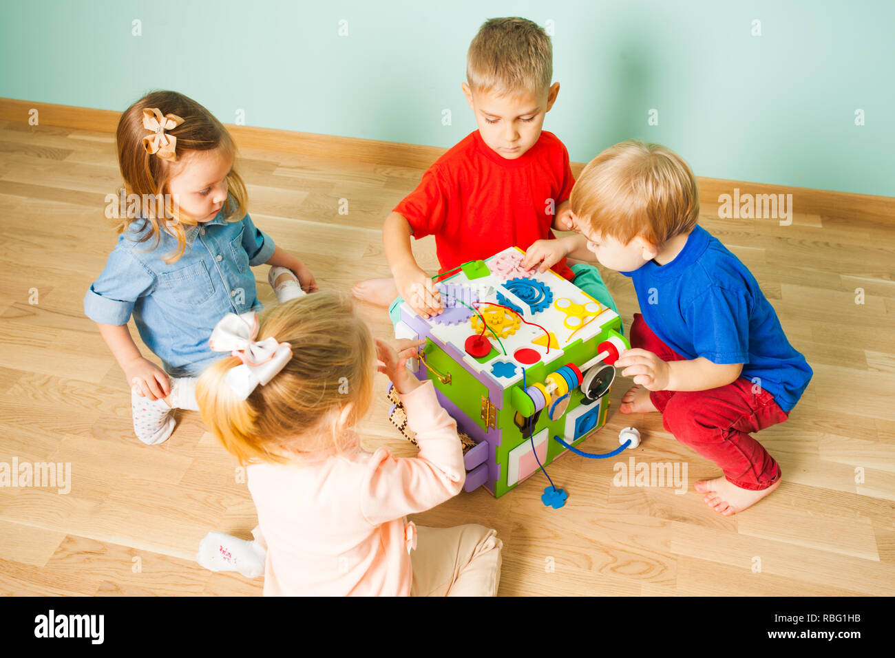 Quatre enfants de maternelle adorable jouant avec l'éducation toy occupé cube, assis sur un sol en bois. Vue de dessus de la formation de leurs enfants les compétences de motilité playi Banque D'Images
