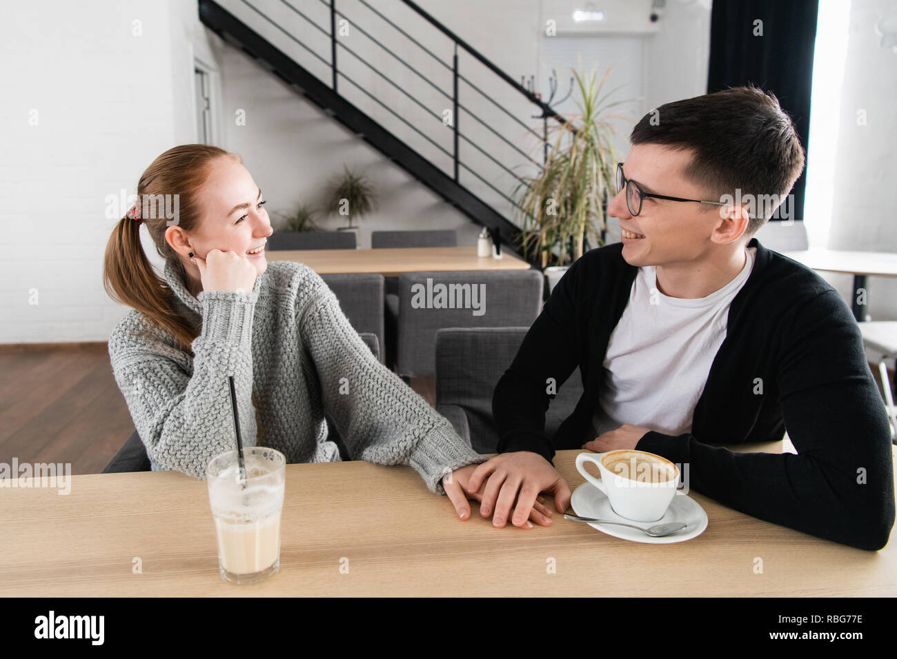 Photo de happy young couple holding hands, regardant et souriant alors qu'il était assis au café Banque D'Images