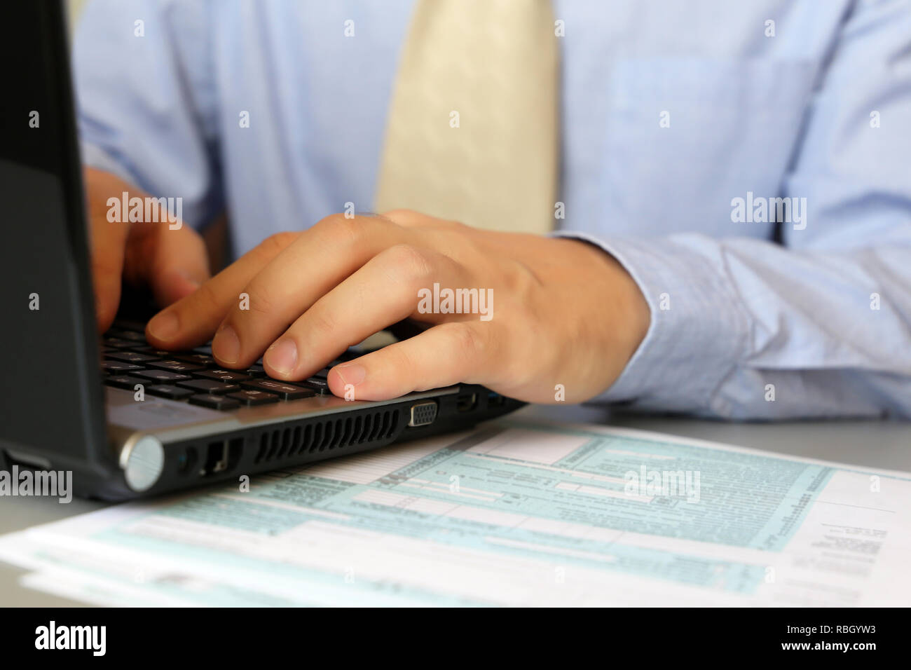 L'homme en chemise bleue et cravate, assis à une table avec un ordinateur portable. Les mains des hommes de taper au clavier, du concept d'office manager, la dotation, l'achèvement de l'at Banque D'Images