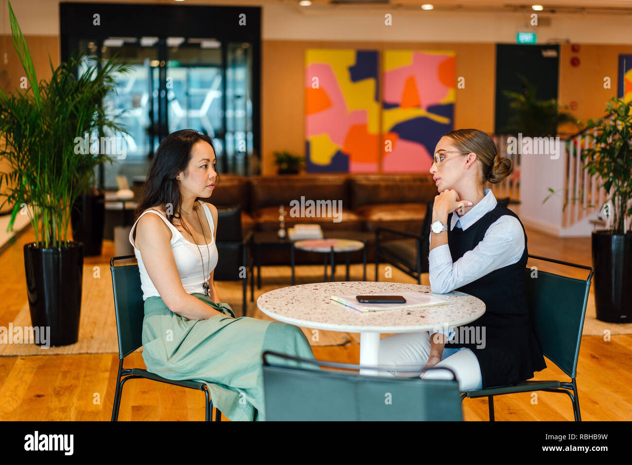 Deux jeunes femmes ont une réunion ensemble dans un bureau pendant la journée. Ils sont d'une équipe diversifiée, l'un est de race blanche, l'autre chinois. Banque D'Images
