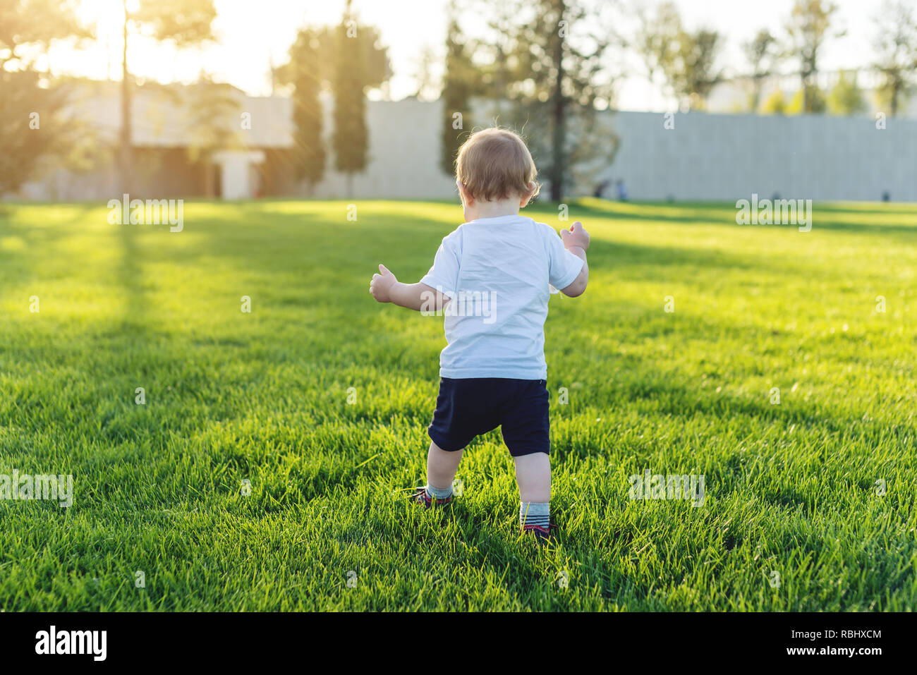 Mignon bébé fonctionne sur une pelouse verte en rattrapage, dans la nature sur une journée ensoleillée. Le concept de un an et les premiers pas de l'enfant Banque D'Images