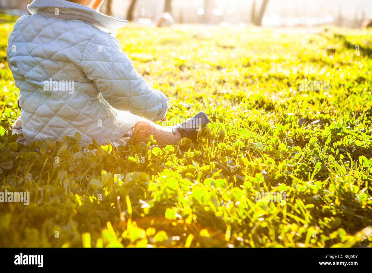 9 mois bébé sous les rayons du soleil sur l'herbe du parc. Avantages de la lumière du soleil pour les bébés concept Banque D'Images