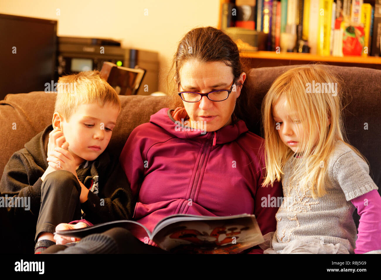 Une maman s'assit sur un canapé-lit un livre à ses deux jeunes enfants Banque D'Images