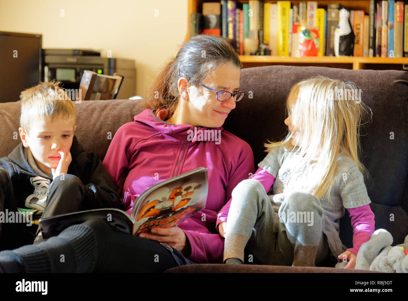 Une maman s'assit sur un canapé-lit un livre à ses deux jeunes enfants Banque D'Images