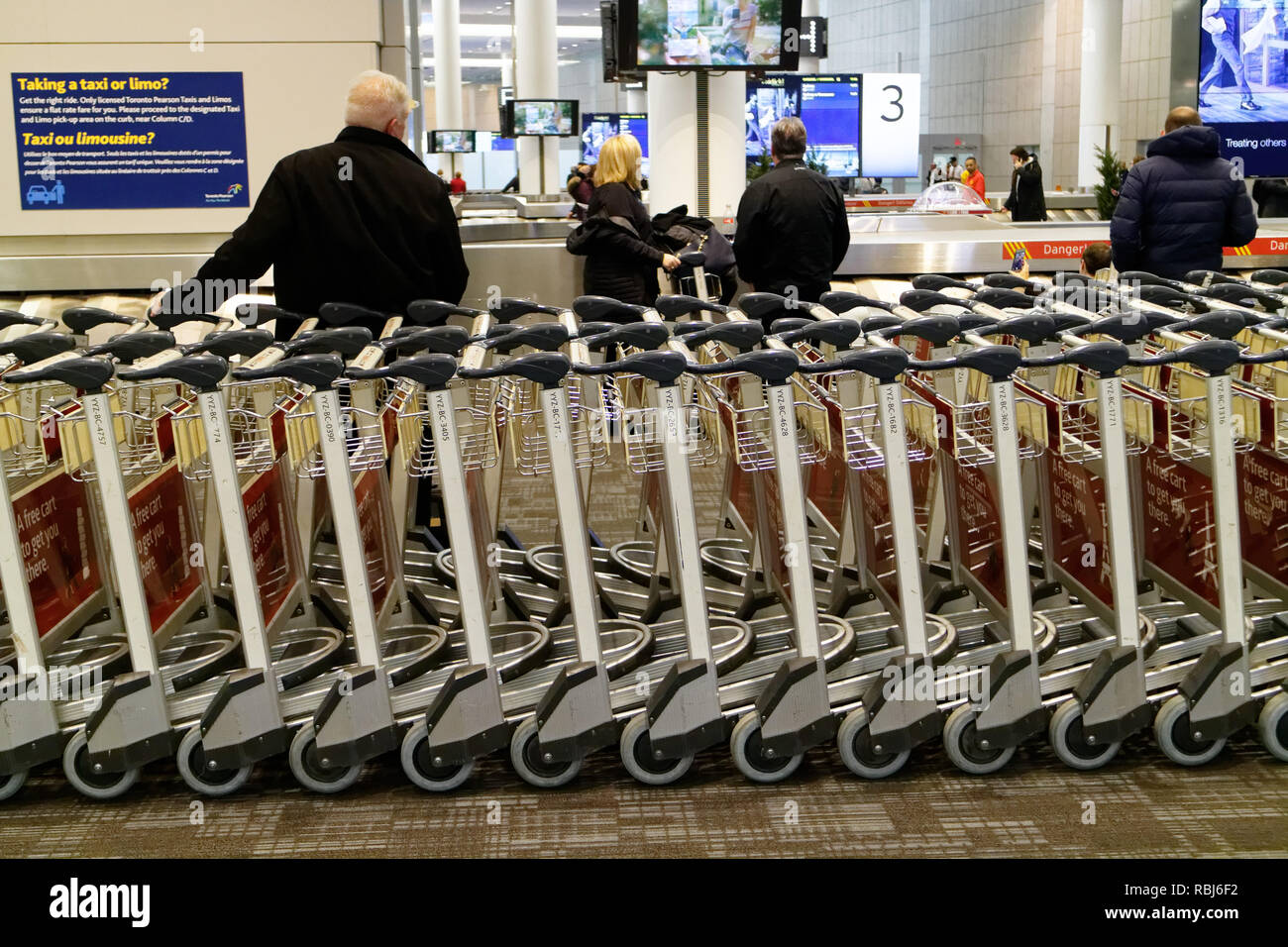 Personnes debout par des rangées de chariots à bagages à l'aéroport Pearson de Toronto en attente de leurs bagages pour arriver. Banque D'Images