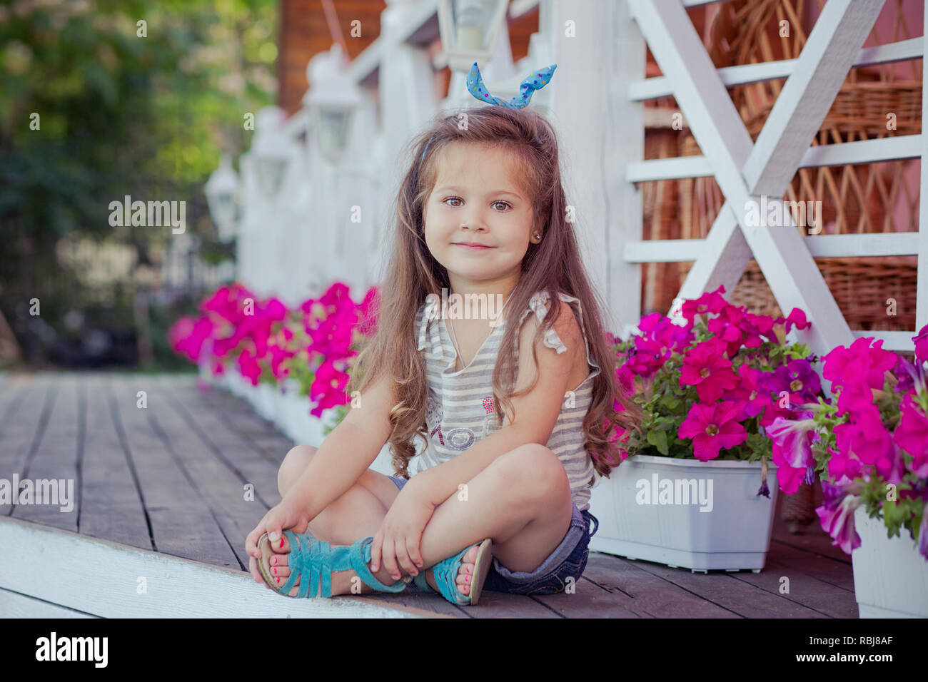Belle élégante cute baby girl avec brunette posing on wooden cheveux jardin  plein de fleurs portant des jeans shirts minuscules et aéré skivy  underwaist et b Photo Stock - Alamy