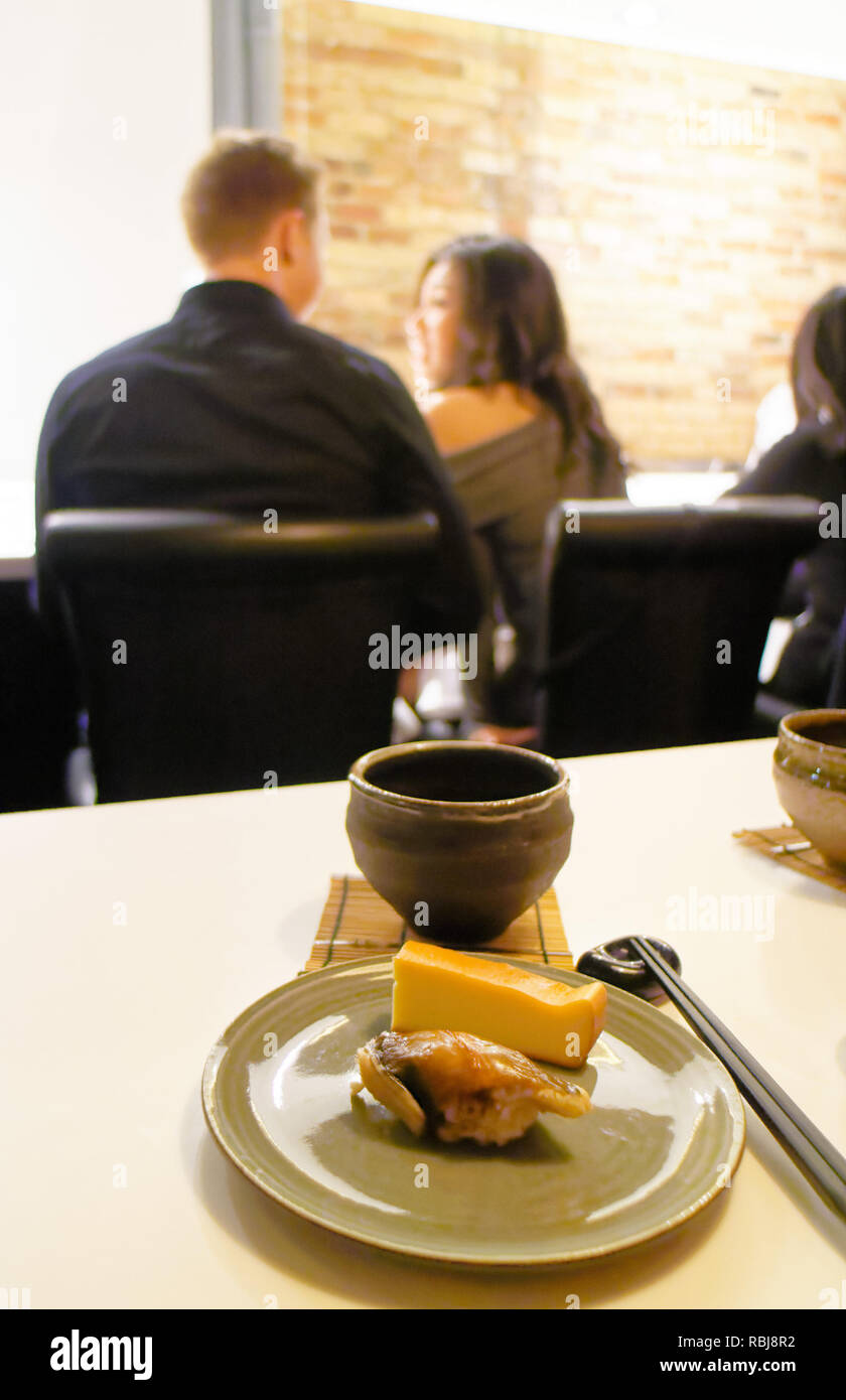 Une plaque d'anguille de mer (Anago)et tamago sushi avec un bol de saké à Yasu Omakase Sushi Bar à Toronto, Canada Banque D'Images