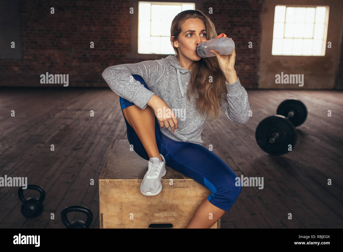 Femme assise sur une boîte à gym après son entraînement et l'eau potable à partir de la bouteille. Prise femelle reste après la formation de remise en forme à la salle de sport. Banque D'Images