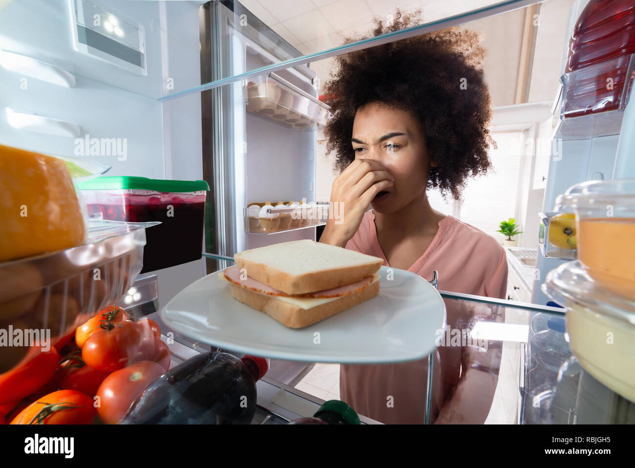 Jeune femme coupe mauvaise odeur de sandwich au jambon près de réfrigérateur à la maison Banque D'Images