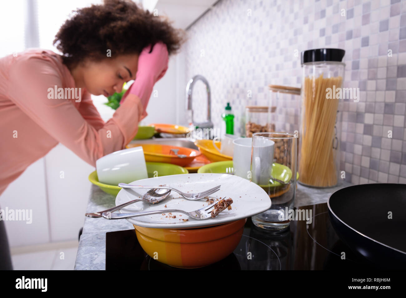 Assez jeune femme se penchant près de l'évier avec des ustensiles colorés sales dans la cuisine Banque D'Images