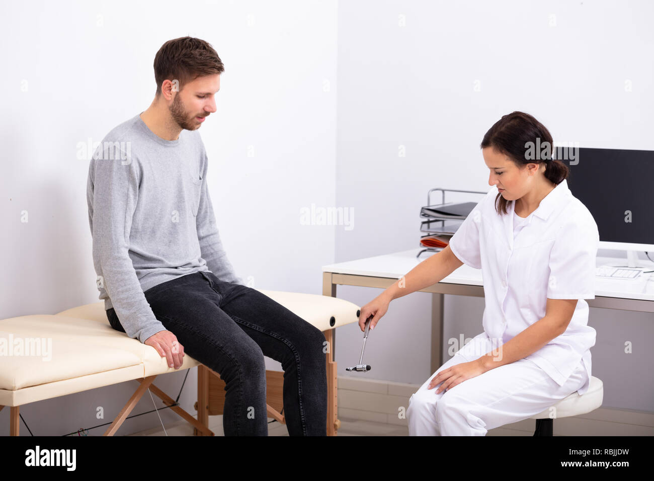 Jeune femme médecin contrôle réflexes du genou de patient de sexe masculin avec un marteau Réflexe Banque D'Images