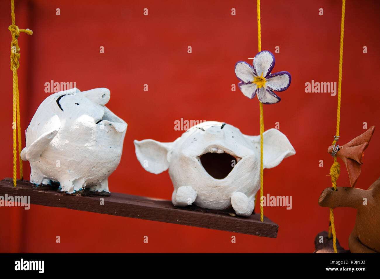 Deux figures d'argile blanche sur une balançoire en face d'un mur rouge Banque D'Images