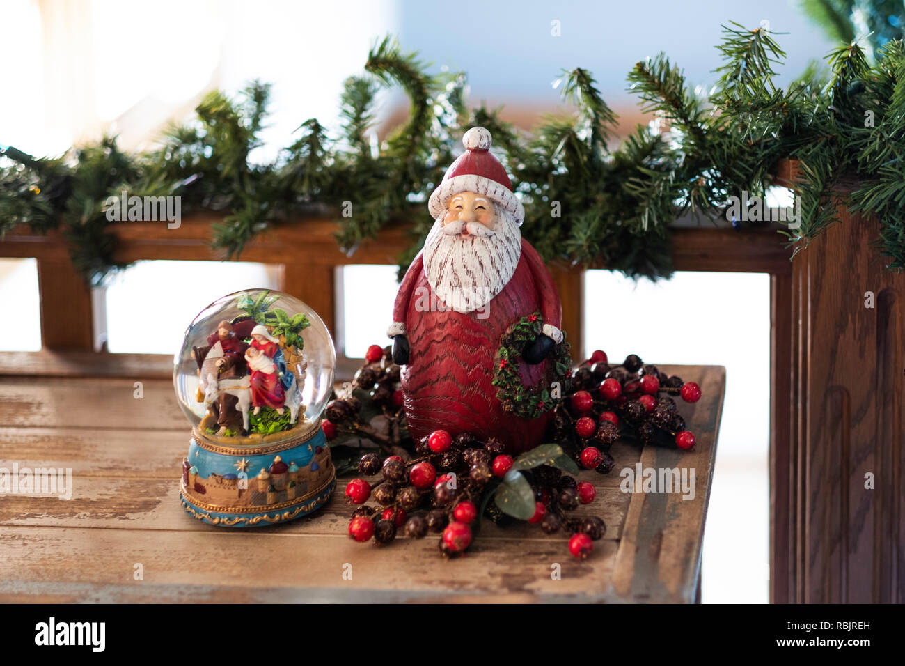 Décorations de Noël, une boule à neige avec crèche vivante et Santa Clause sur une table en bois avec garland sur une balustrade. Banque D'Images